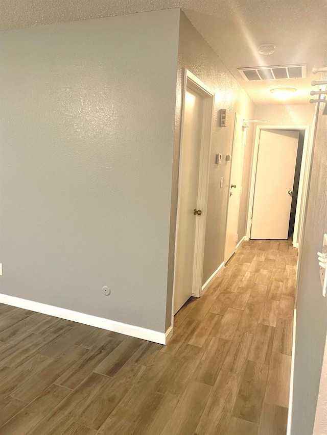 hall with light wood-type flooring, baseboards, and visible vents