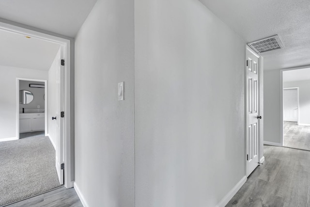 hallway featuring visible vents, a textured ceiling, baseboards, and wood finished floors