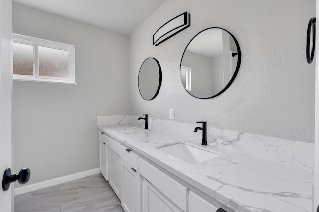 bathroom featuring marble finish floor, double vanity, a sink, and baseboards