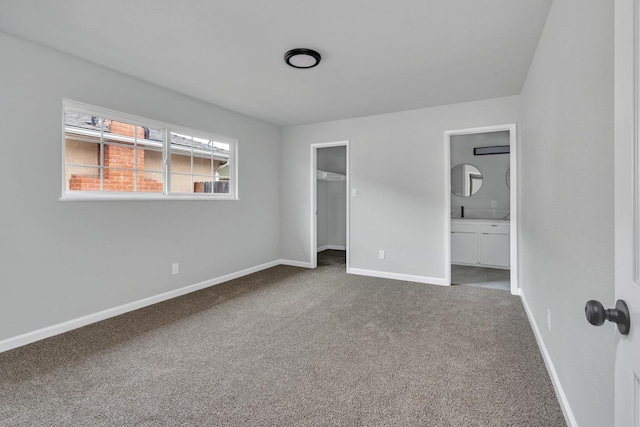 unfurnished bedroom with carpet flooring, baseboards, a closet, a walk in closet, and ensuite bath