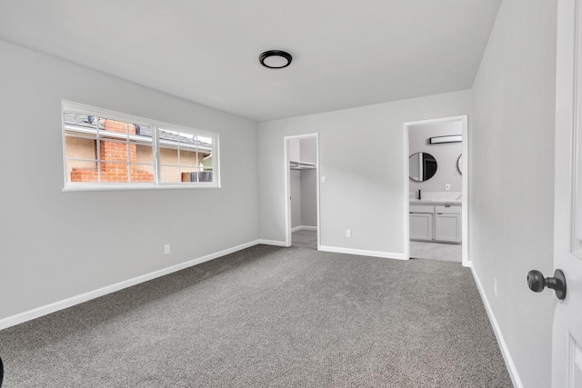 unfurnished bedroom featuring carpet floors, a closet, a spacious closet, ensuite bathroom, and baseboards