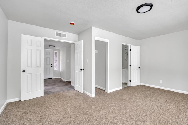 unfurnished bedroom featuring a textured ceiling, carpet, visible vents, and baseboards