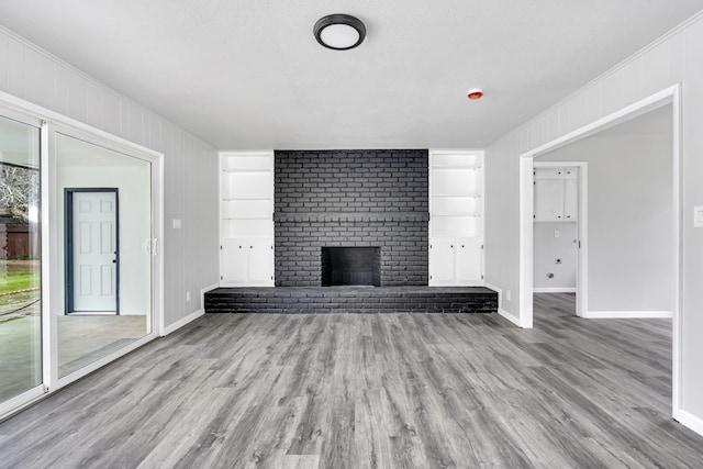 unfurnished living room featuring built in shelves, a fireplace, wood finished floors, and baseboards