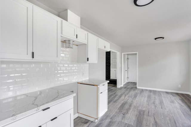 kitchen featuring light wood-style flooring, decorative backsplash, white cabinets, light stone countertops, and baseboards