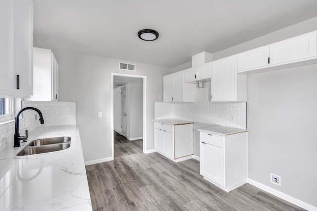 kitchen featuring baseboards, visible vents, light stone countertops, light wood-type flooring, and a sink