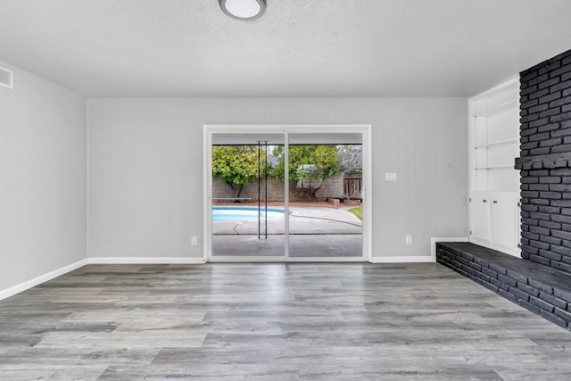 unfurnished living room with visible vents, a textured ceiling, baseboards, and wood finished floors