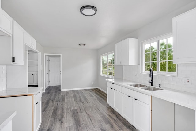 kitchen featuring tasteful backsplash, white cabinetry, a sink, wood finished floors, and baseboards