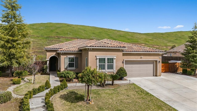 mediterranean / spanish-style home featuring a garage, a tile roof, fence, and stucco siding