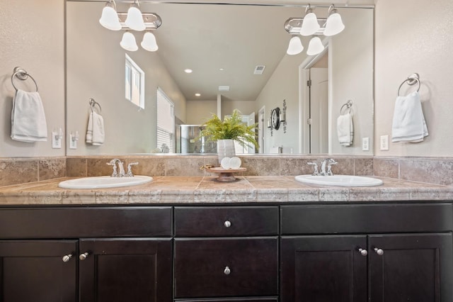 full bathroom with double vanity, a shower with shower door, visible vents, and a sink