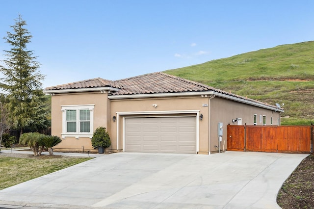 mediterranean / spanish home featuring a garage, fence, a tiled roof, and stucco siding