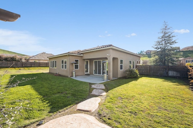 rear view of house featuring a fenced backyard, a tile roof, a lawn, stucco siding, and a patio area