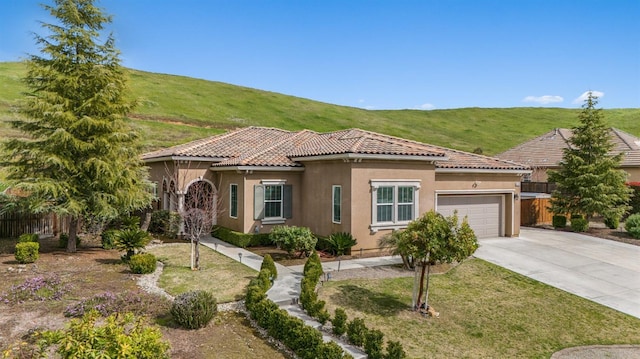 mediterranean / spanish-style house with concrete driveway, a tile roof, stucco siding, an attached garage, and fence