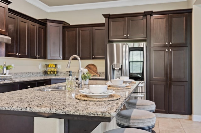 kitchen featuring light stone counters, a breakfast bar area, dark brown cabinetry, a sink, and ornamental molding