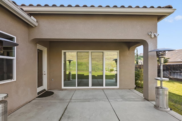 doorway to property featuring a patio area, fence, a tiled roof, and stucco siding