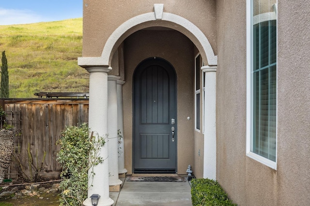 view of exterior entry featuring fence and stucco siding