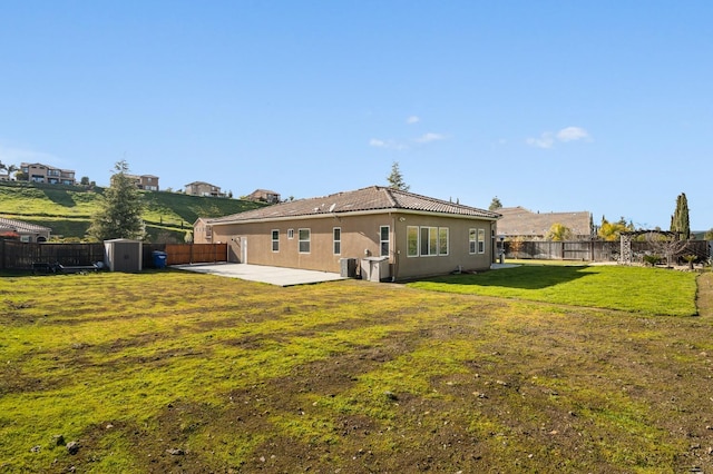 back of house featuring a storage shed, a lawn, a fenced backyard, a tiled roof, and an outbuilding