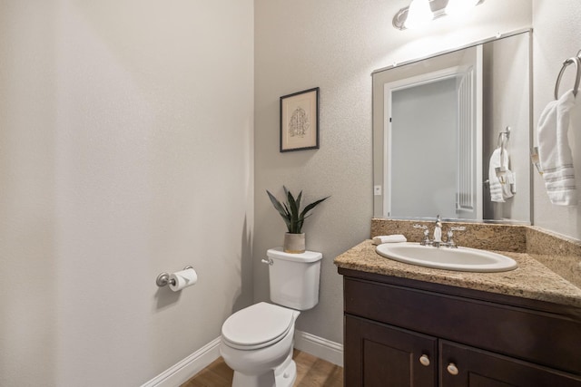 bathroom featuring toilet, vanity, wood finished floors, and baseboards