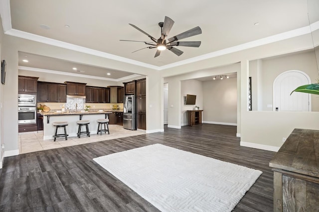 living area featuring baseboards, ceiling fan, ornamental molding, light wood-type flooring, and recessed lighting