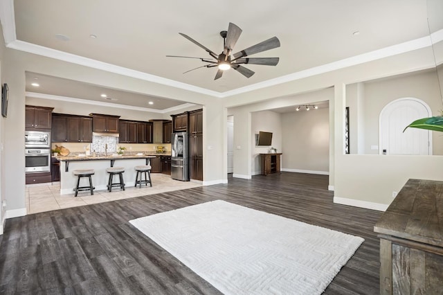 living room featuring recessed lighting, light wood-type flooring, crown molding, a ceiling fan, and baseboards