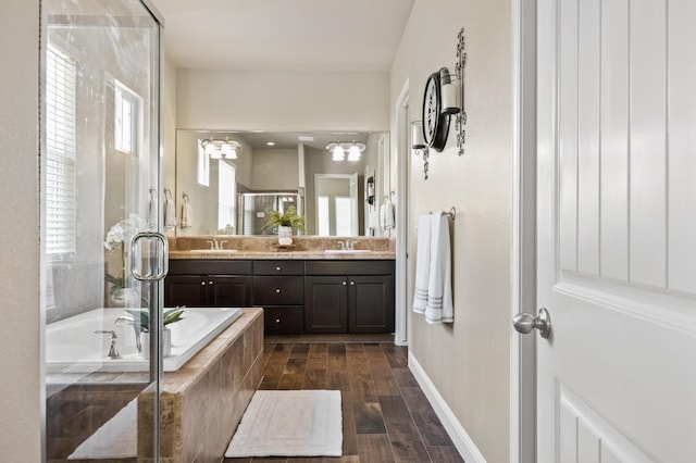 bathroom featuring wood finished floors, a shower stall, double vanity, a bath, and a sink