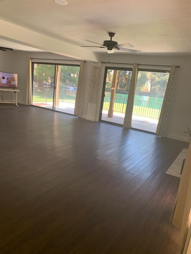 empty room featuring a ceiling fan, dark wood finished floors, and baseboards