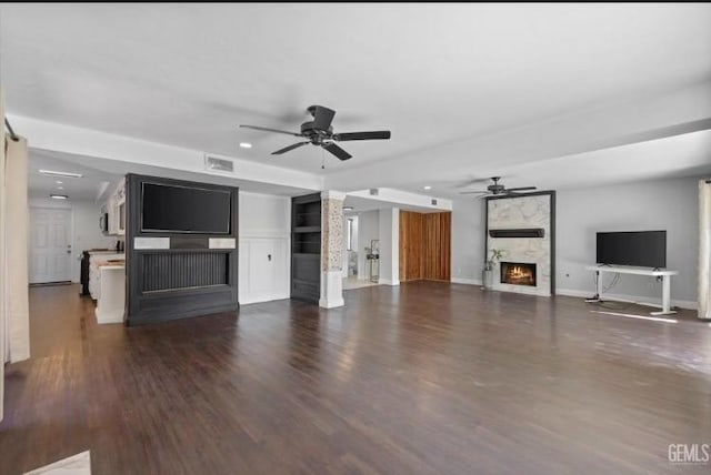 unfurnished living room with dark wood finished floors, visible vents, a ceiling fan, a large fireplace, and baseboards