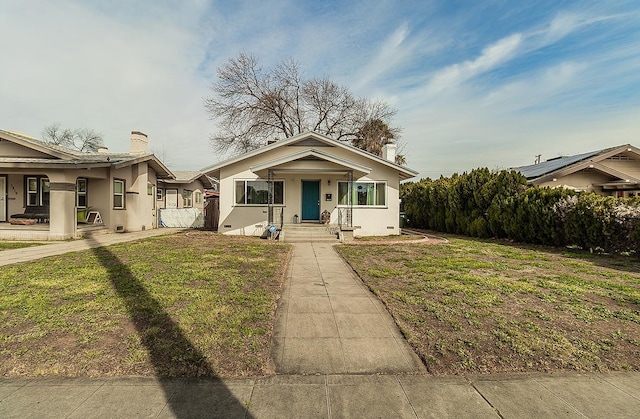 bungalow-style house featuring a front yard, a chimney, fence, and stucco siding