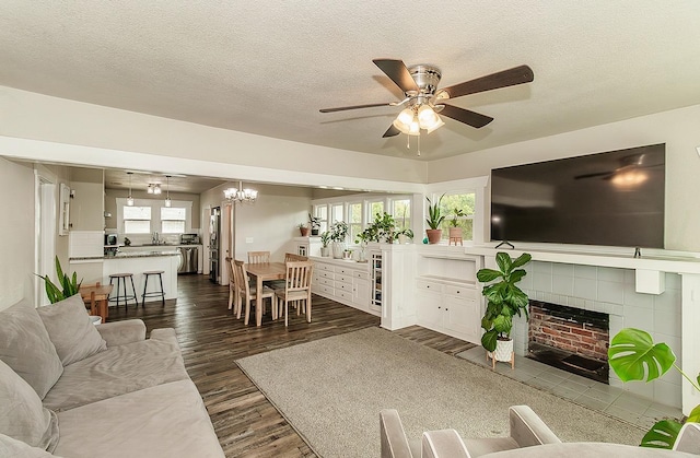 living area with dark wood finished floors, wine cooler, a textured ceiling, a fireplace, and ceiling fan with notable chandelier