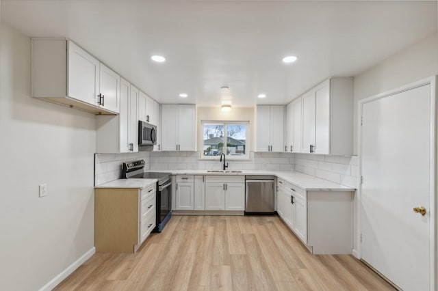 kitchen with decorative backsplash, appliances with stainless steel finishes, a sink, and light wood finished floors