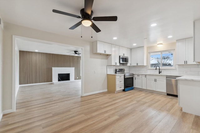 kitchen with light wood finished floors, tasteful backsplash, ceiling fan, light countertops, and appliances with stainless steel finishes