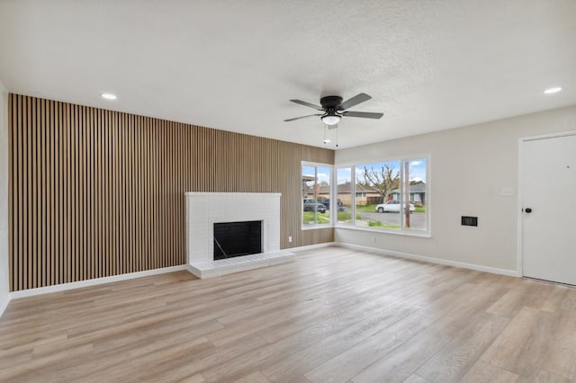 unfurnished living room featuring ceiling fan, a textured ceiling, baseboards, a brick fireplace, and light wood finished floors