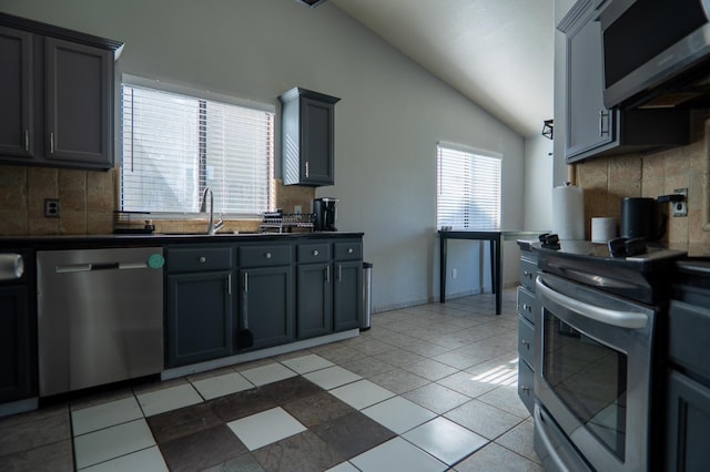 kitchen with decorative backsplash, dark countertops, vaulted ceiling, stainless steel appliances, and a sink