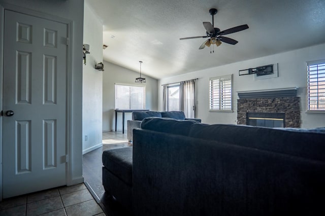 living area featuring ceiling fan, tile patterned floors, vaulted ceiling, a textured ceiling, and a fireplace