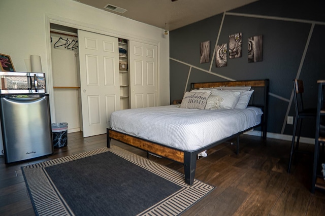 bedroom featuring a closet, wood finished floors, visible vents, and refrigerator