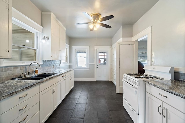 kitchen featuring a sink, white cabinetry, white gas range oven, decorative backsplash, and dark stone countertops