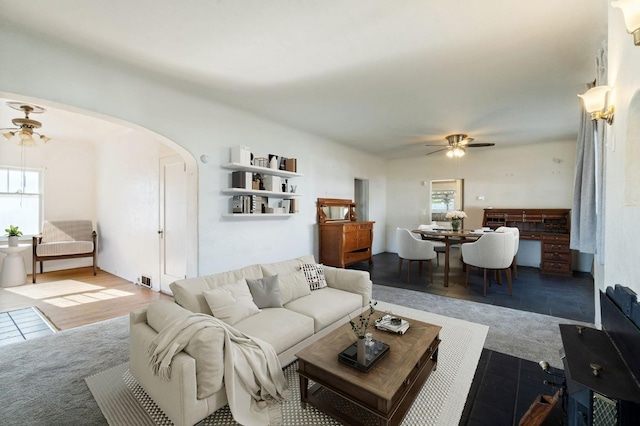 carpeted living room with a ceiling fan, arched walkways, and a healthy amount of sunlight