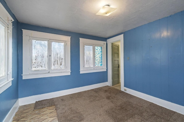 carpeted empty room featuring a textured ceiling and baseboards