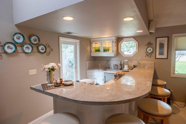 kitchen with visible vents, dishwasher, a breakfast bar, a peninsula, and a wealth of natural light