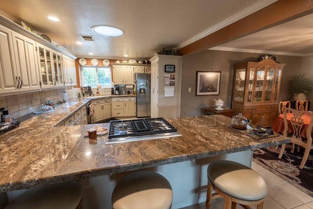 kitchen with decorative backsplash, a kitchen breakfast bar, tile patterned floors, stainless steel appliances, and cream cabinetry