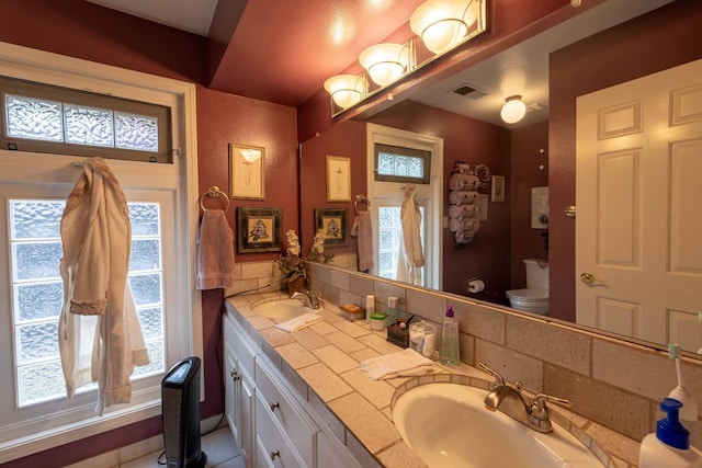 full bath with toilet, double vanity, visible vents, and a sink