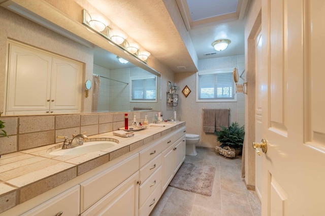 full bathroom with toilet, decorative backsplash, a sink, and tiled shower