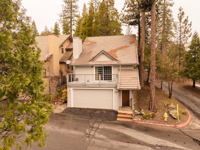 view of front of house featuring a balcony, a tile roof, a chimney, aphalt driveway, and an attached garage