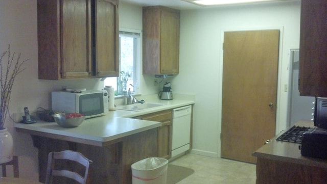 kitchen featuring a breakfast bar area, a peninsula, white appliances, a sink, and light countertops