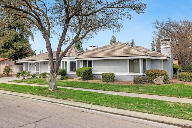 ranch-style home with a chimney, stucco siding, a front yard, fence, and a garage