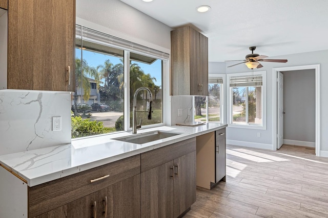 kitchen featuring baseboards, decorative backsplash, ceiling fan, light wood-style flooring, and a sink