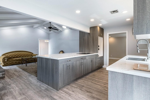 kitchen featuring light wood finished floors, visible vents, a ceiling fan, a sink, and a peninsula