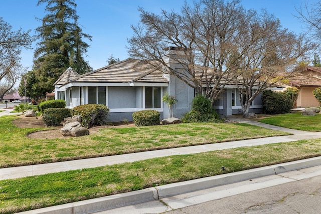 view of front of property featuring stucco siding, a tile roof, a chimney, and a front yard