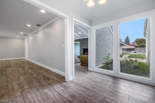 interior space featuring a fireplace, wood finished floors, visible vents, baseboards, and crown molding