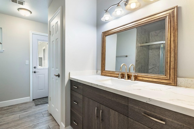 bathroom with a marble finish shower, visible vents, vanity, wood finished floors, and baseboards