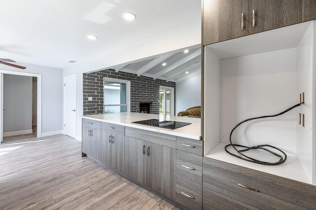 kitchen featuring a fireplace, light wood finished floors, light countertops, a ceiling fan, and black electric cooktop